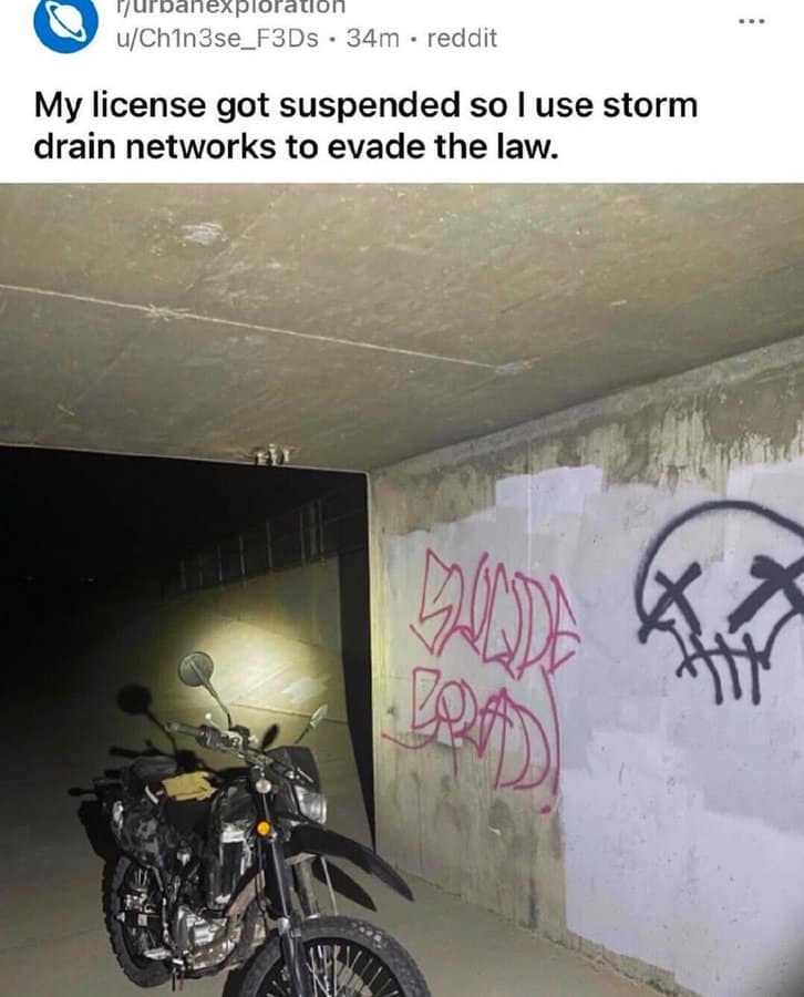 A screenshot from r/urbanexploration showing a dirt bike parked in a pitch-black concrete storm drain, with the user admitting they use the sewer tunnels to commute after their license was suspended.