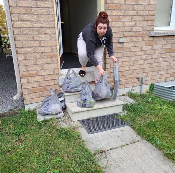 A woman crouches on her front steps to grab several plastic bags of groceries.