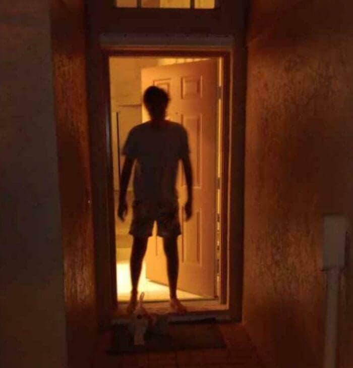 A dark, grainy photo of a person silhouetted in a doorway like a horror movie villain.