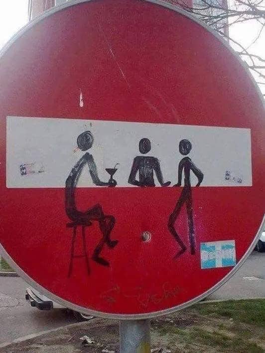 Creative graffiti on a road sign transforms a do-not-enter symbol into a bar counter scene.