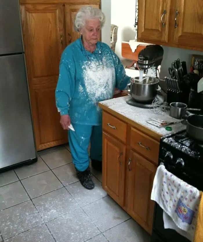 Candid photo of an elderly woman covered in white flour while using a stand mixer.