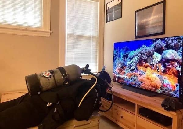 Person lying on a bench in full scuba gear watching a coral reef documentary on television.