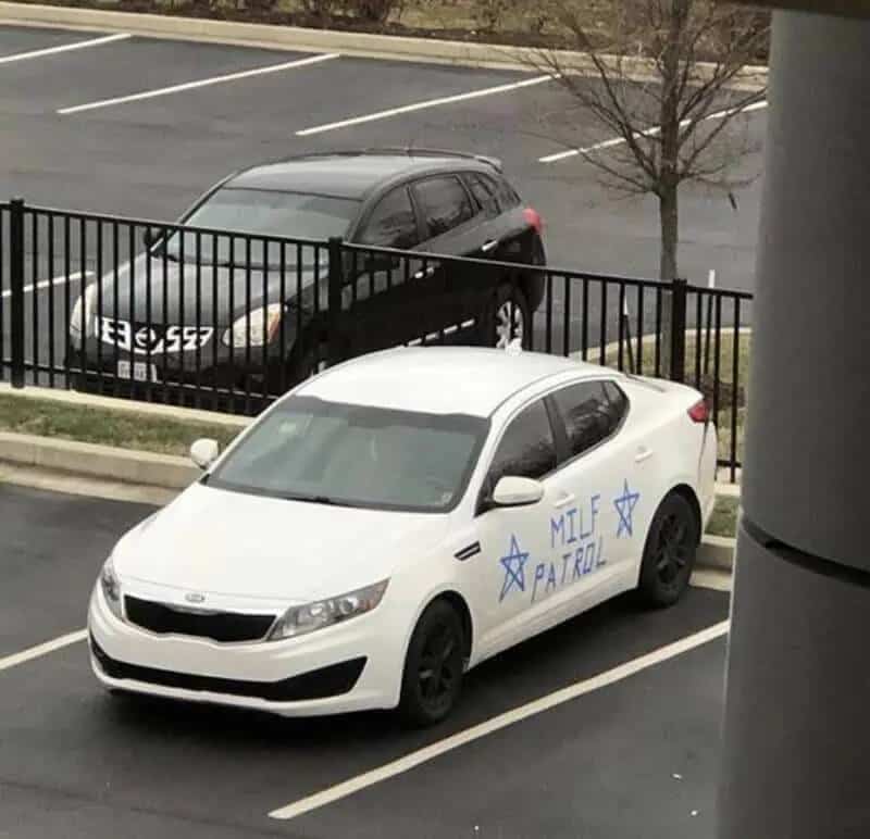 A white Kia sedan parked in a lot with a custom blue MILF Patrol decal.
