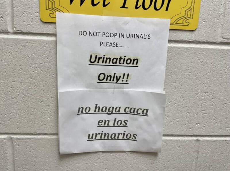 Humorous public restroom sign in English and Spanish explicitly telling users not to poop in the urinals.