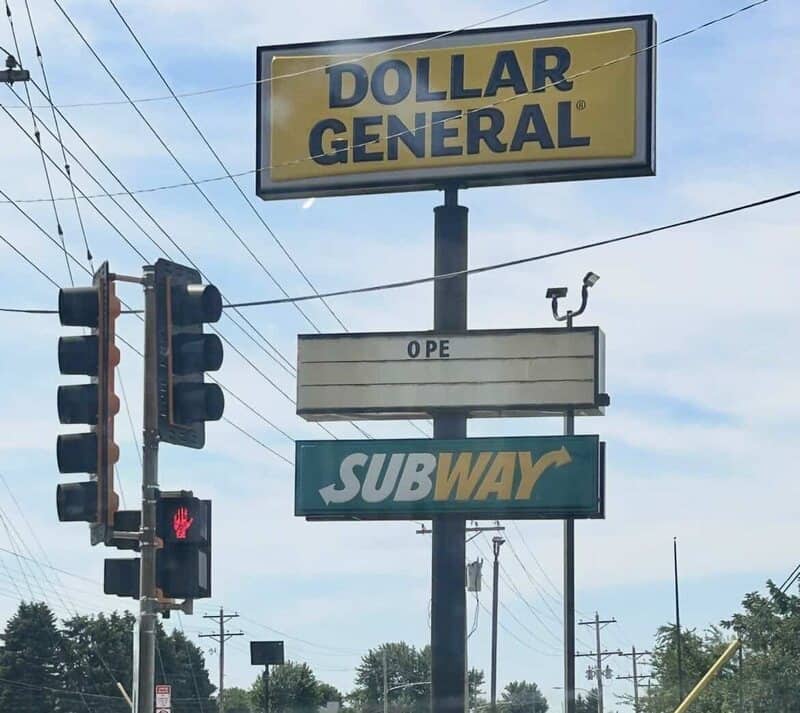 Street sign for Dollar General and Subway with a custom middle sign reading Ope.