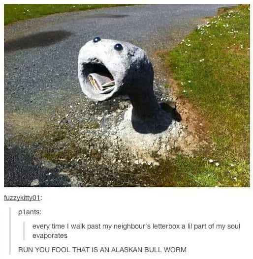Funny outdoor letterbox shaped like a gray monster head with its mouth open to receive mail.