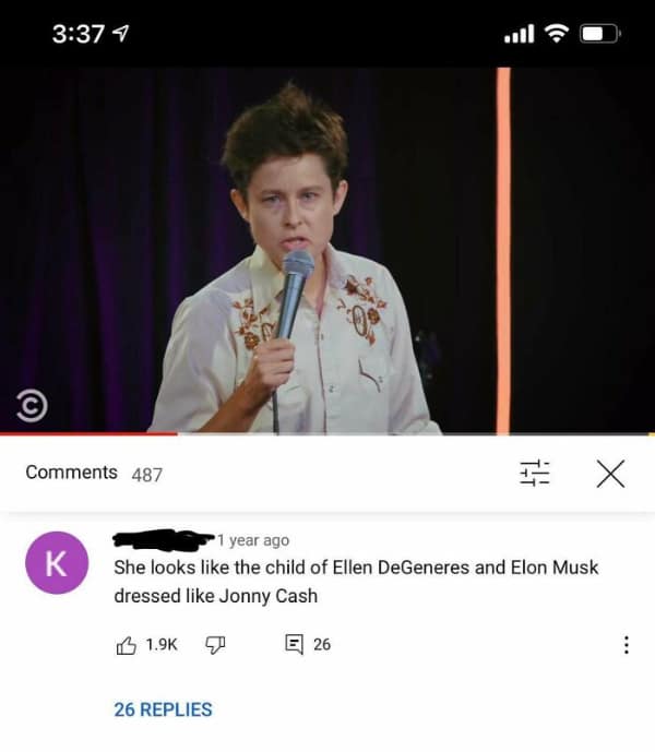 A screenshot of a stand-up comedian performing on stage. The comment section features a specific funny roast that describes the performer as the hypothetical child of Ellen DeGeneres and Elon Musk wearing a Johnny Cash outfit.