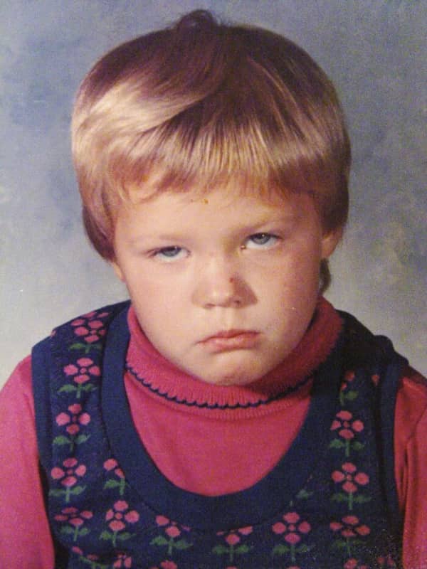 A young child with a bowl cut wearing a pink turtleneck looks intensely annoyed.