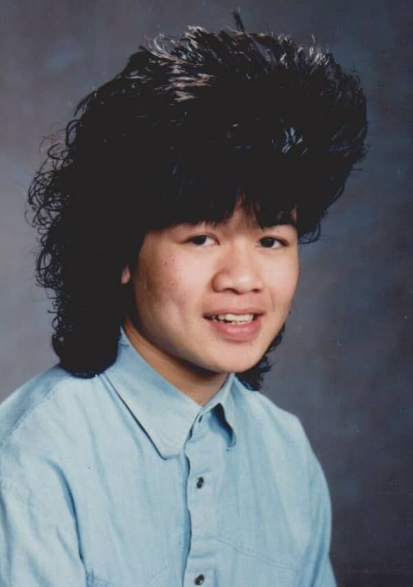 Teenager with an incredibly voluminous, feathered black hairstyle smiling for a school portrait.