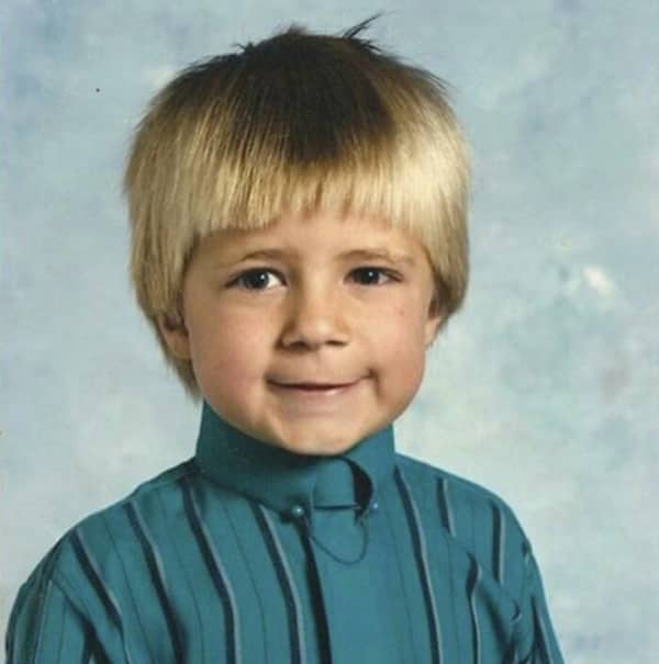 A young boy with an extremely straight bowl cut wears a teal striped shirt.