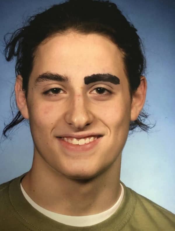 A smiling teenage boy has one regular eyebrow and one thickly drawn black eyebrow.