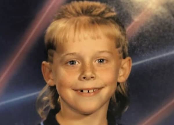 Young child smiling with a dramatic blonde mullet haircut against a laser background.