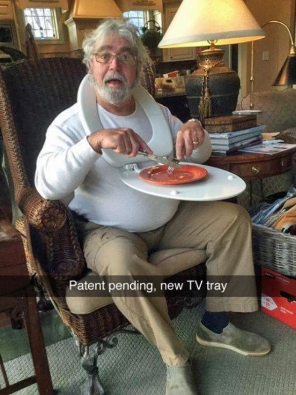 Elderly man wearing a toilet seat around his neck as a makeshift TV tray.