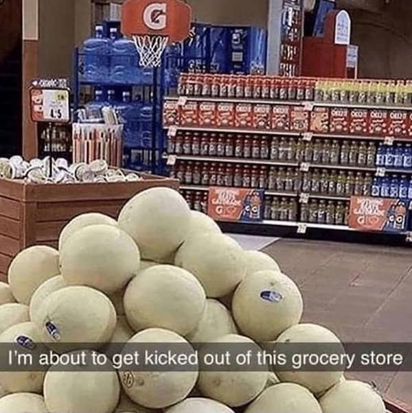 A stack of melons in a grocery store with a basketball hoop display overhead.