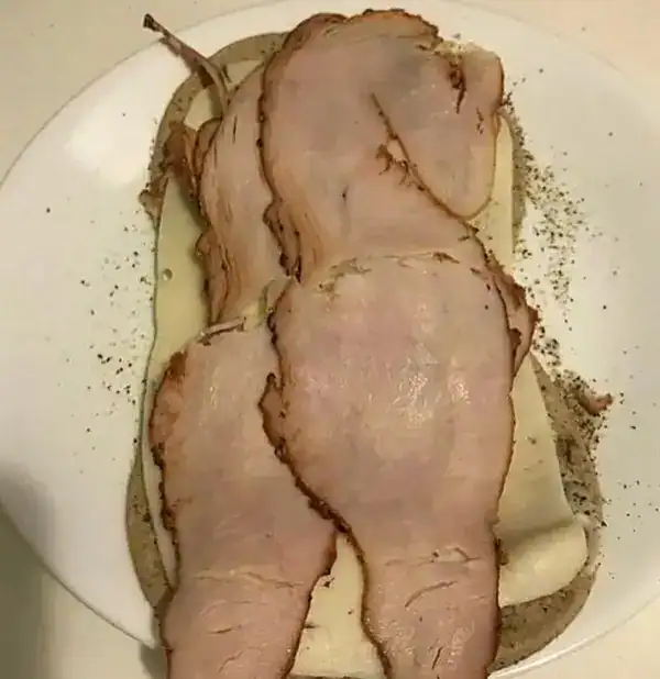 Slices of ham and cheese arranged on a plate resembling a human body silhouette.