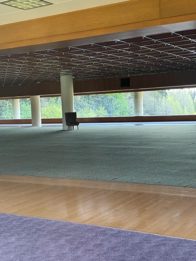 An isolated armchair sits next to a massive concrete pillar inside an empty, carpeted corporate event hall, showcasing the unsettling silence of eerie liminal spaces