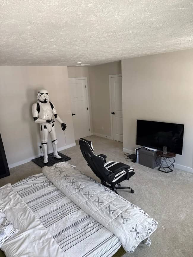 A bedroom setup featuring a gaming chair positioned in the middle of the floor facing away from a life-sized Stormtrooper statue.