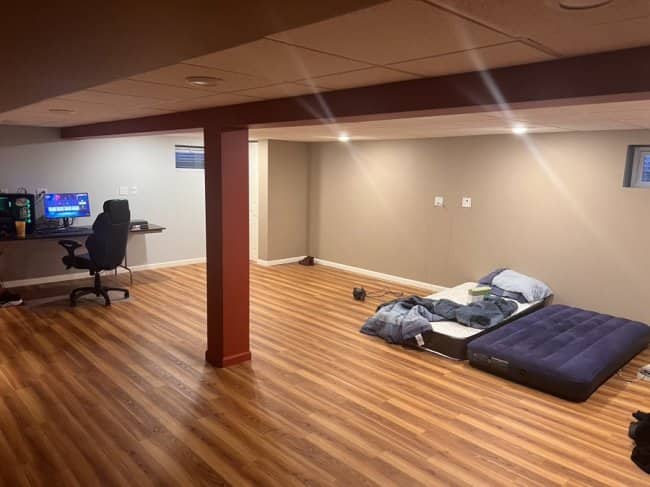 A vast basement room featuring an air mattress, a regular mattress on the floor, and a complete computer desk setup.