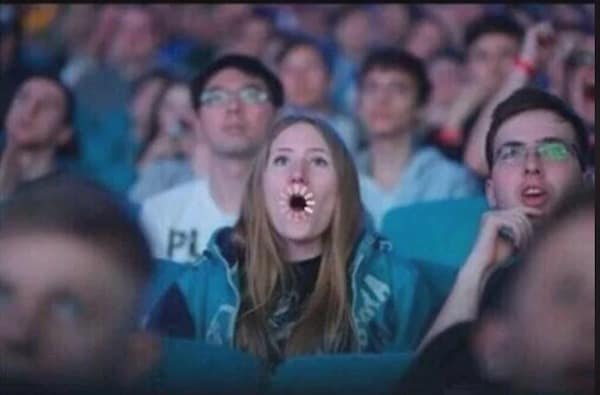 A stunned woman in a crowded theater audience is captured with a digital buffering wheel photoshopped over her wide-open mouth in a viral meme dump entry about slow internet speeds.