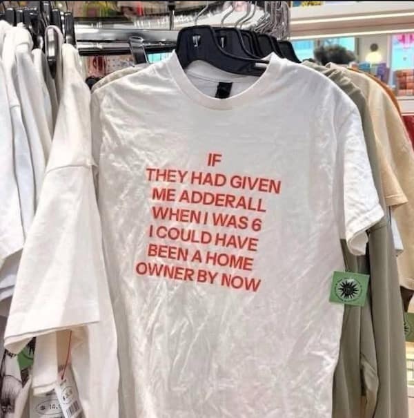 A white graphic t-shirt on a retail clothing rack displays bold red text reading "If they had given me Adderall when I was 6 I could have been a home owner by now," featured in a trending meme dump.