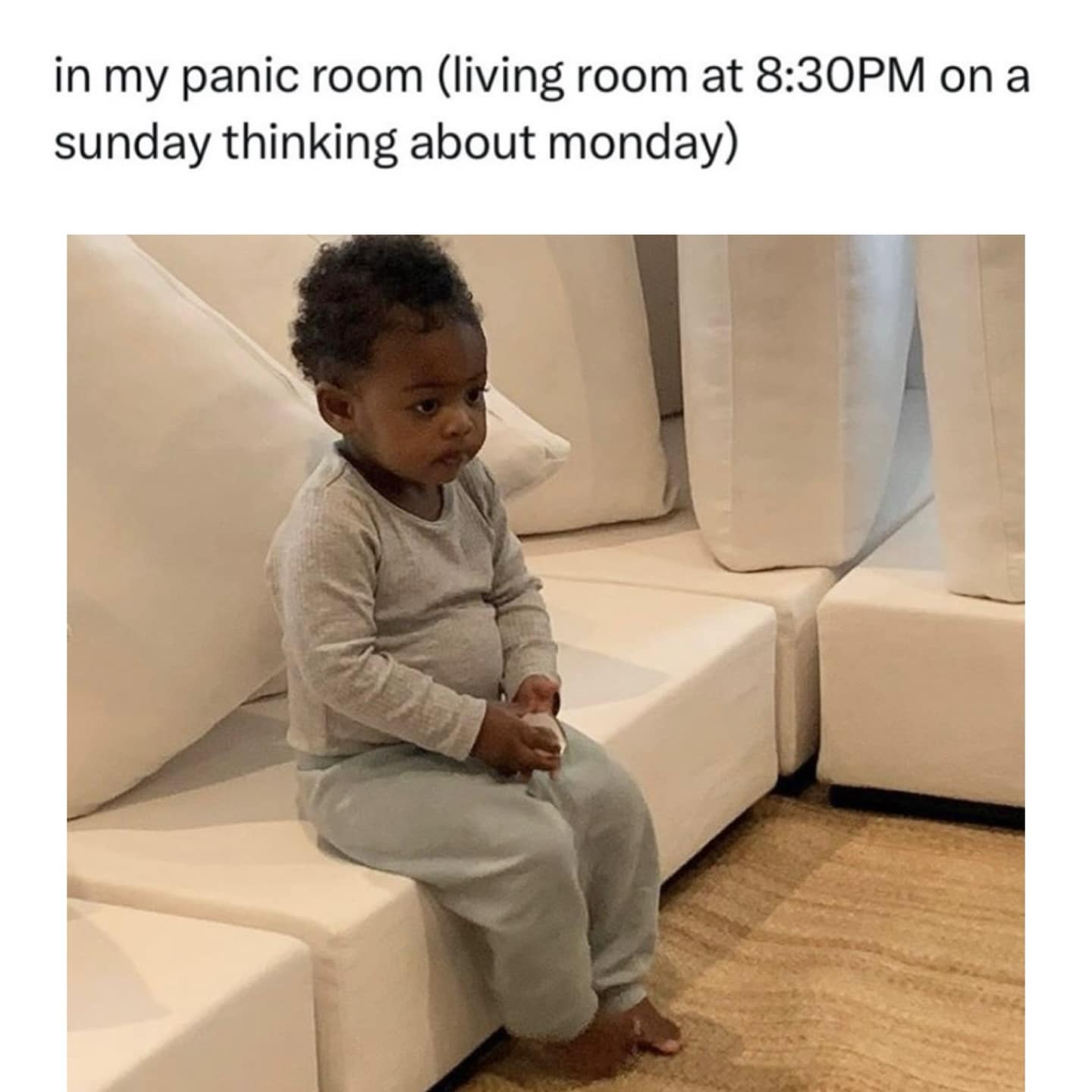 A relatable hilarious meme showing a small toddler sitting on the edge of a massive white designer sofa with a thousand-yard stare, captioned: "in my panic room (living room at 8:30PM on a sunday thinking about monday)."
