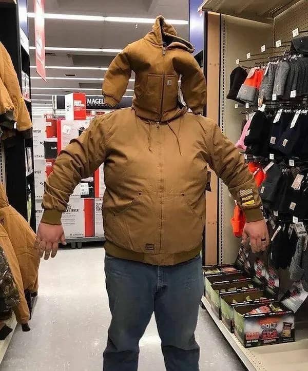 A surreal meme dump visual of a person in a store wearing a heavy brown Carhartt work jacket with a second, smaller jacket pulled over their head like a mask, creating a terrifying "workwear golem" aesthetic.