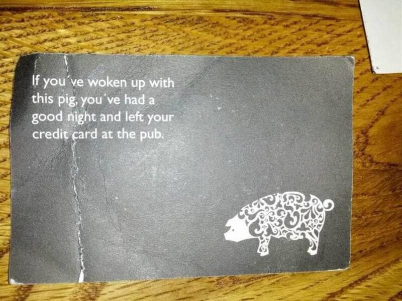 A printed black card from a bar or pub featuring a white decorative silhouette of a swine alongside text warning that waking up with the card means you left your credit card behind after a wild night.