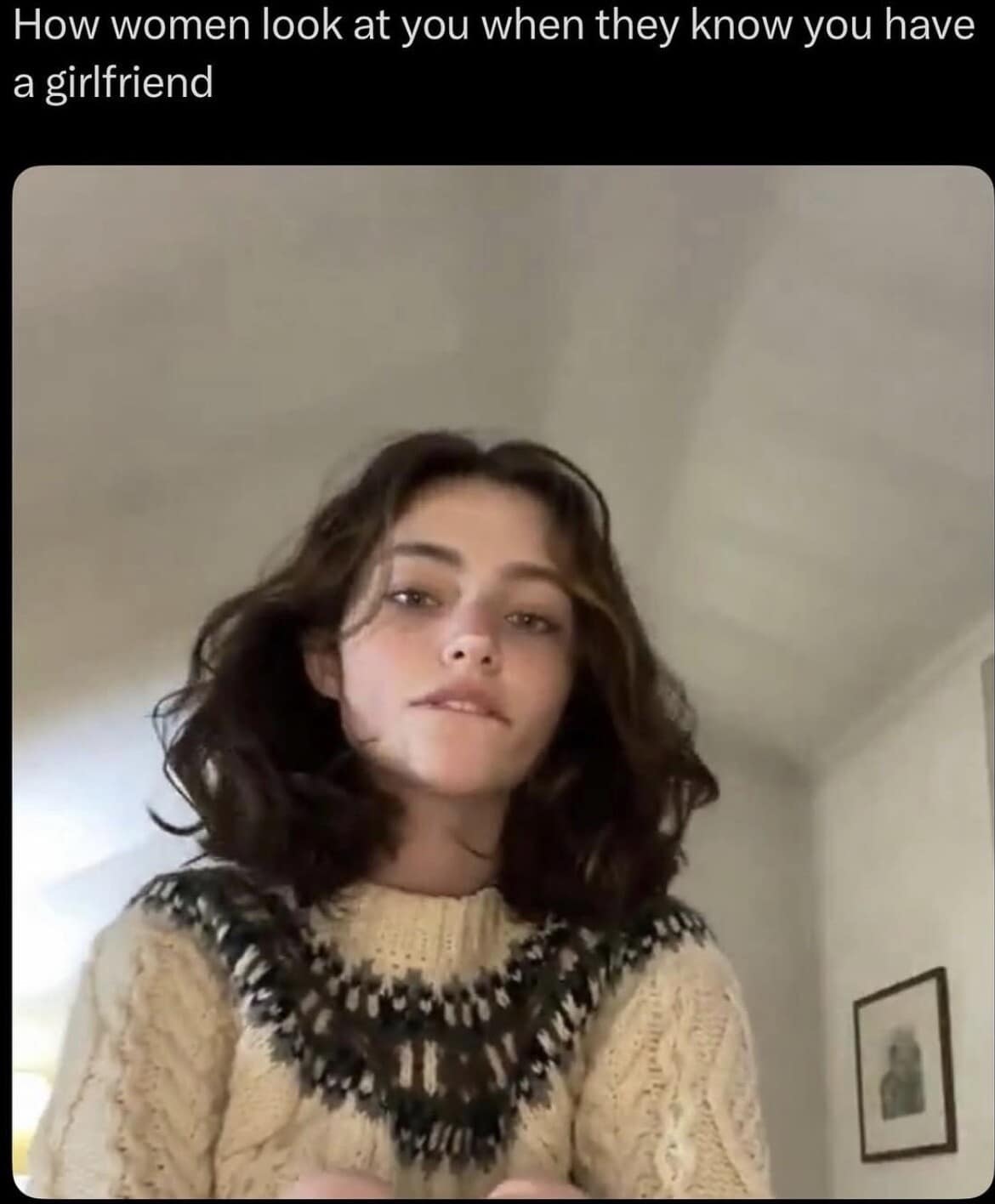 A funny meme featuring a young woman in a patterned sweater biting her lip and looking toward the camera with an intense, predatory gaze, captioned "How women look at you when they know you have a girlfriend."