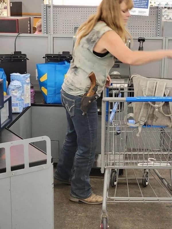 A candid, high-octane photo of a woman shopping at Walmart with a massive, long-barreled wooden-handled revolver holstered on her hip, embodying the peak of "main character" grocery store energy.