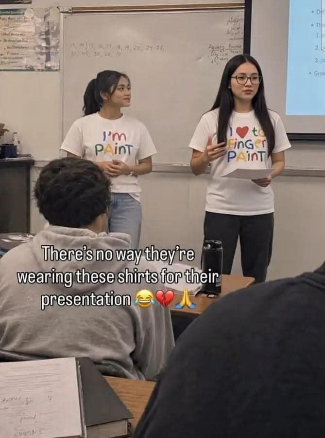 A viral meme dump photo showing two students giving a classroom presentation wearing matching white t-shirts that, when standing together, create a hilariously and accidentally inappropriate sentence about "finger painting."