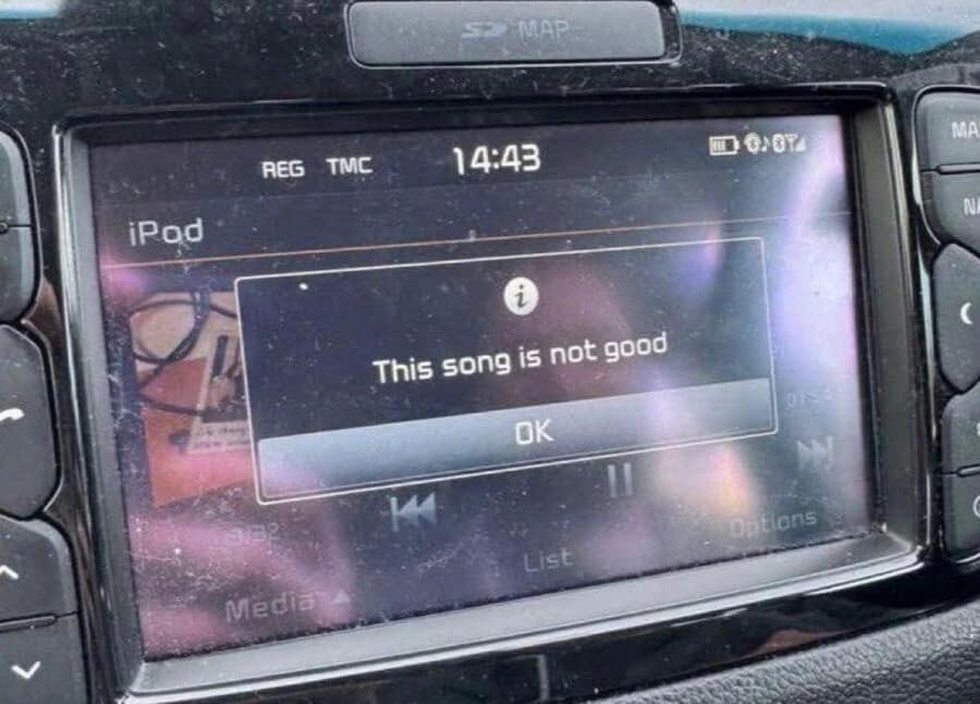 A dusty in-car infotainment dashboard system displays a brutally honest, custom system warning pop-up box stating "This song is not good" over an OK button prompt.
