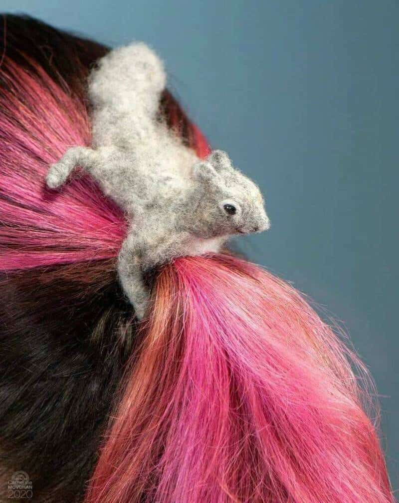 A bizarre hair accessory photo showing a realistic gray felted squirrel that appears to be "clinging" to a woman's vibrant hot-pink ponytail as if it’s a tree branch.