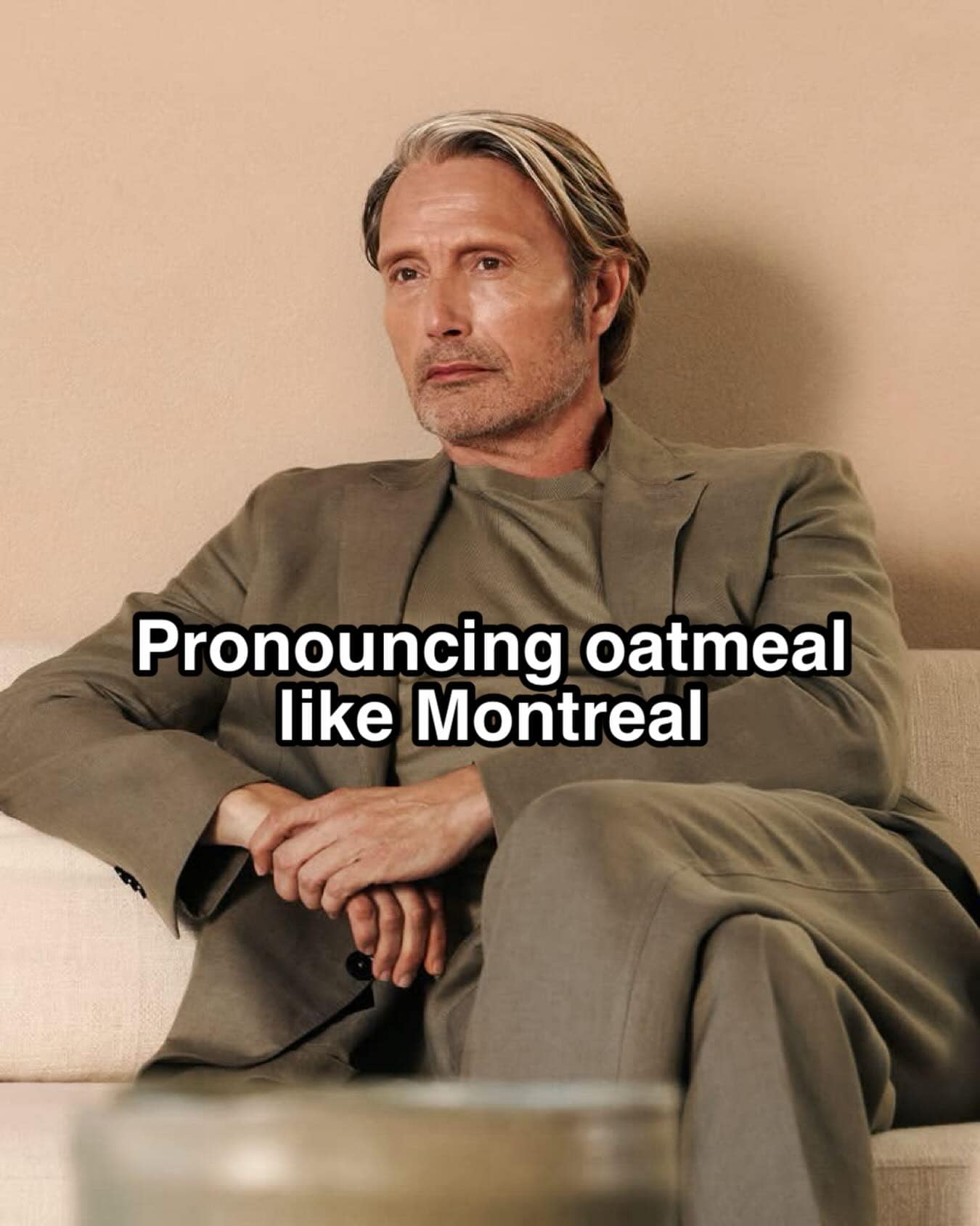 A portrait of a sophisticated, well-dressed Mads Mikkelsen sitting on a sofa anchors an elite linguist meme about pronouncing the word oatmeal with a dramatic French-Canadian Montreal accent.