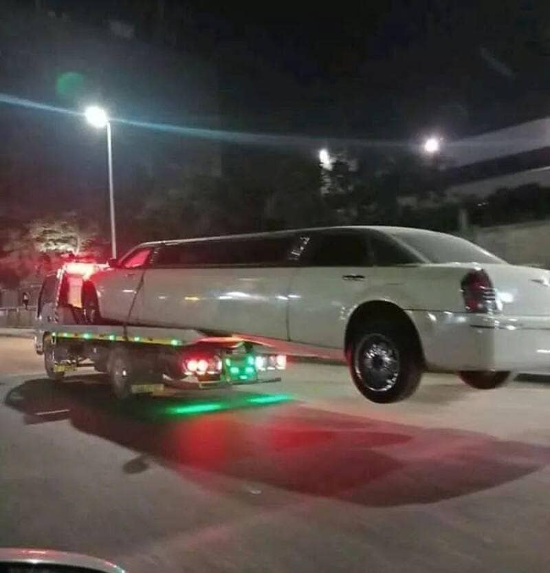 A bizarre nighttime highway photo featured in a popular meme dump shows an oversized white stretch limousine loaded onto a flatbed tow truck with its rear wheels completely suspended in mid-air.