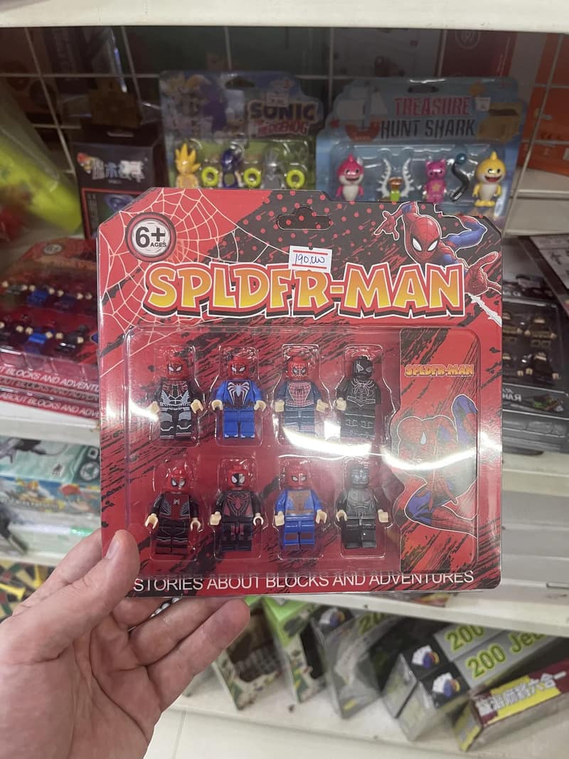 A close-up hand photo highlights a package of bootleg superhero block minifigures, shared in a meme dump because the cardboard header features a major spelling typo reading "SPLDFR-MAN."