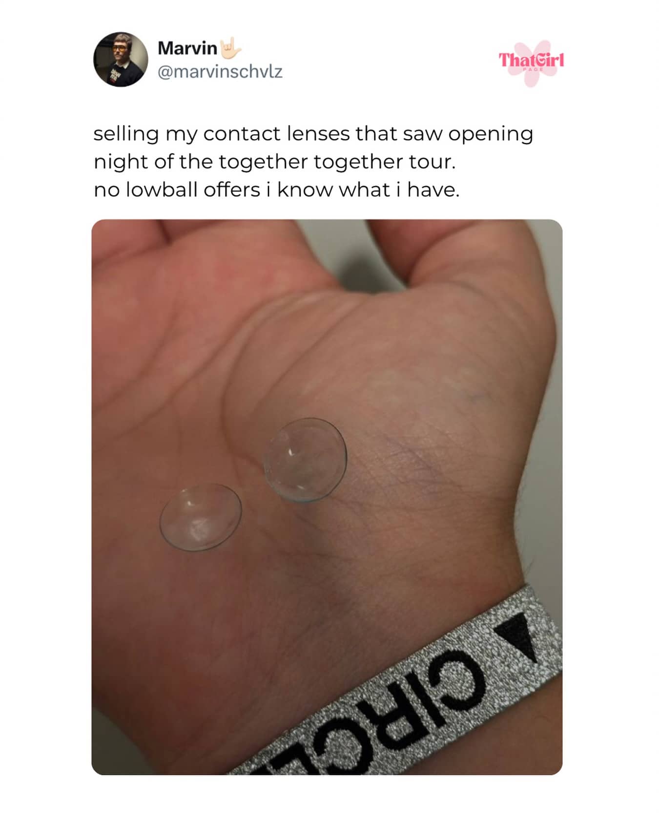 Two clear contact lenses sitting on a person's palm next to a concert wristband.