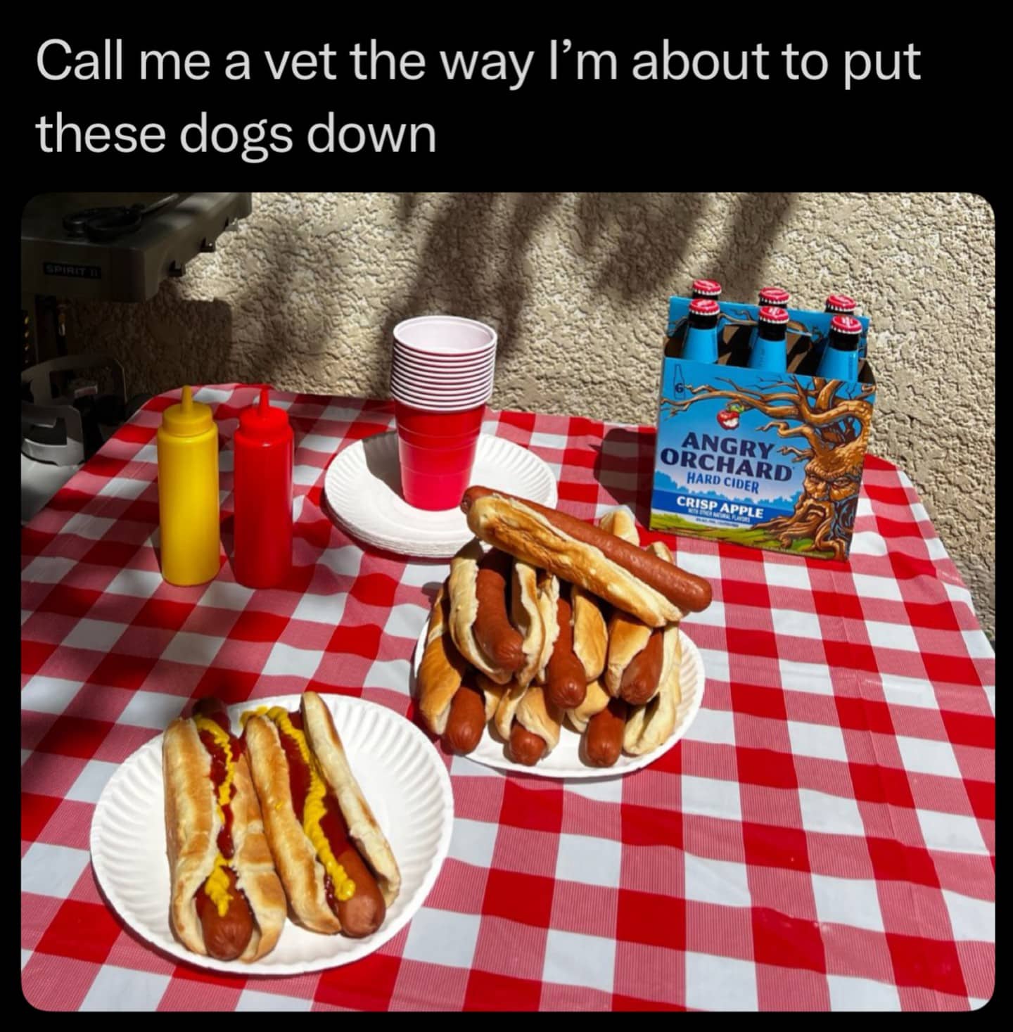 A pile of cooked hot dogs on a red and white checkered picnic table.