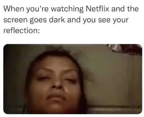 A blurry, low-angle reflection of a woman’s face in a dark TV screen during a Netflix pause.