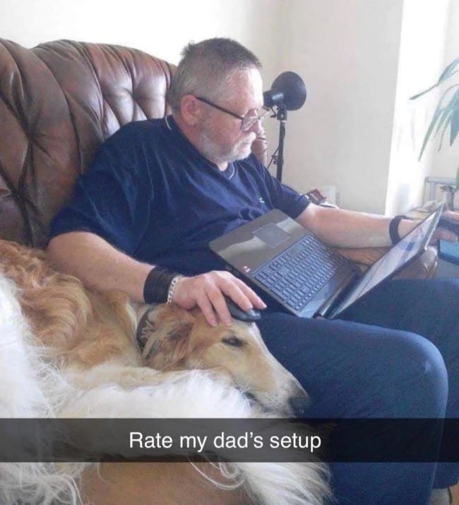 A man sitting on a couch using a long-nosed dog’s head as a makeshift mousepad for his laptop.