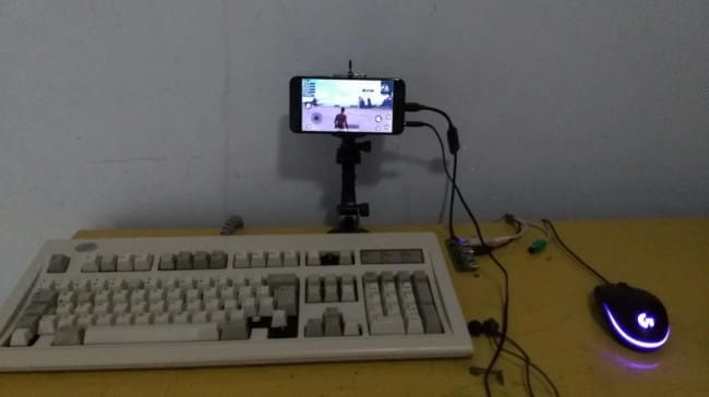 A mobile phone mounted on a tripod acting as a monitor for a full-sized mechanical keyboard and mouse.
