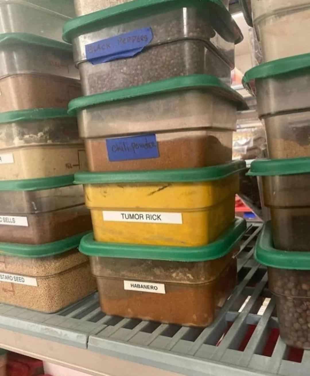 A kitchen spice rack showing a massive spelling fail on a label that reads "TUMOR RICK" on a container filled with bright yellow turmeric powder.