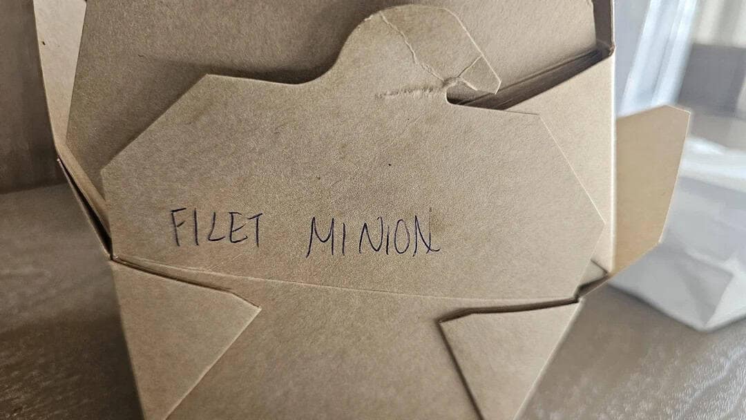 A takeout box with a handwritten spelling fail identifying the contents as "FILET MINION" instead of "Filet Mignon."