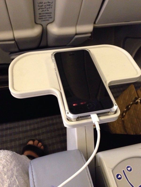 An iPhone sliding smoothly into the exact molded slot of an airplane armrest tray.