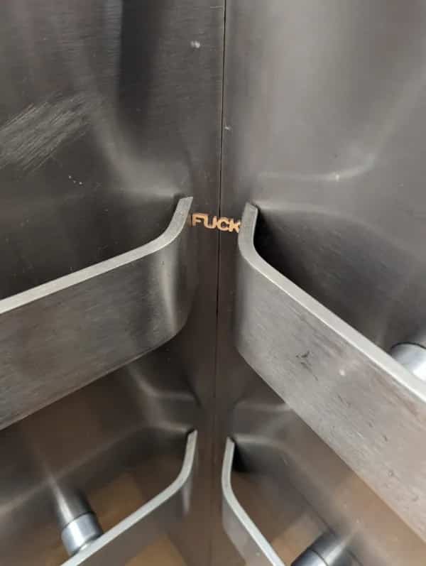 A small plastic swear word toy wedge perfectly into the microscopic corner gap of an elevator handrail.