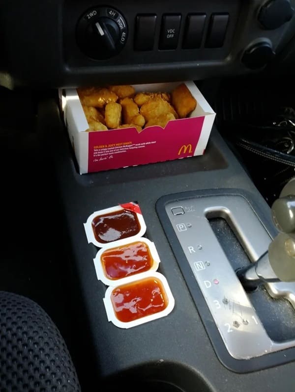 A box of McDonald's chicken nuggets and three sauce packets tucked seamlessly into a car console slot.