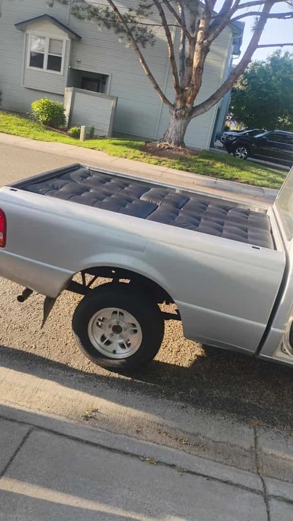 A black quilted mattress fitting tightly and flatly into the entire bed of a silver pickup truck.