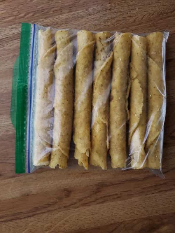 Seven golden taquitos lined up tightly and uniformly inside a clear plastic ziplock bag.
