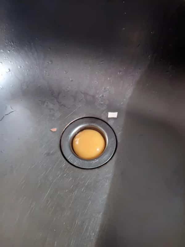 A completely intact raw egg yolk sitting cleanly over a metal kitchen sink drain opening.
