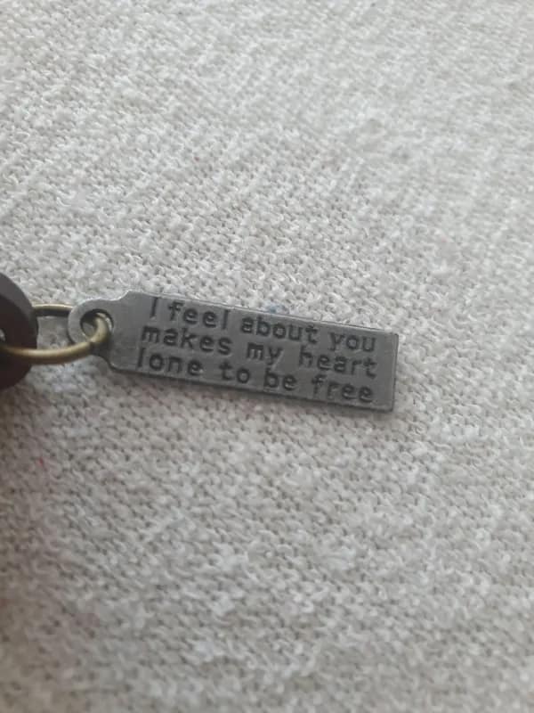 A close-up shot of a metal jewelry tag charm displays a poetic spelling malfunction reading, "I feel about you makes my heart lone to be free," cementing its spot as a viral translation fail.