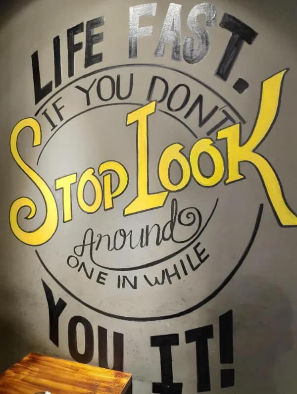 A hand-painted cafe wall quote suffers a complete graphic design and english fail, jumbling a classic pop-culture line into the chaotic word salad text, "LIFE FAST. IF YOU DONT STOP LOOK Around ONE IN WHILE YOU IT!"